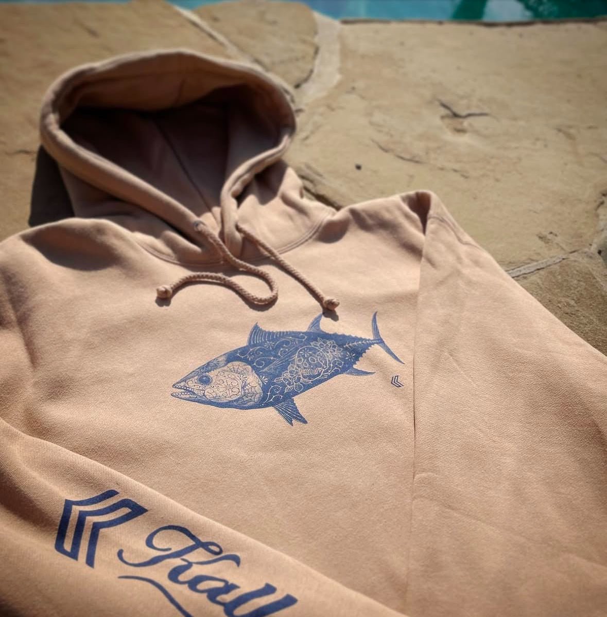 Hooded sweatshirt with tuna art on it laying on rocks