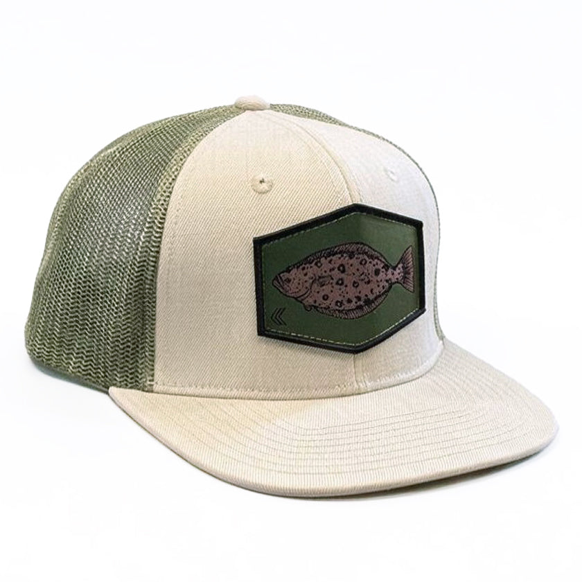 A trucker-style baseball cap with a cream-colored front panel and visor, olive green mesh back panels, and a dark green hexagonal patch featuring a halibut design on the front.